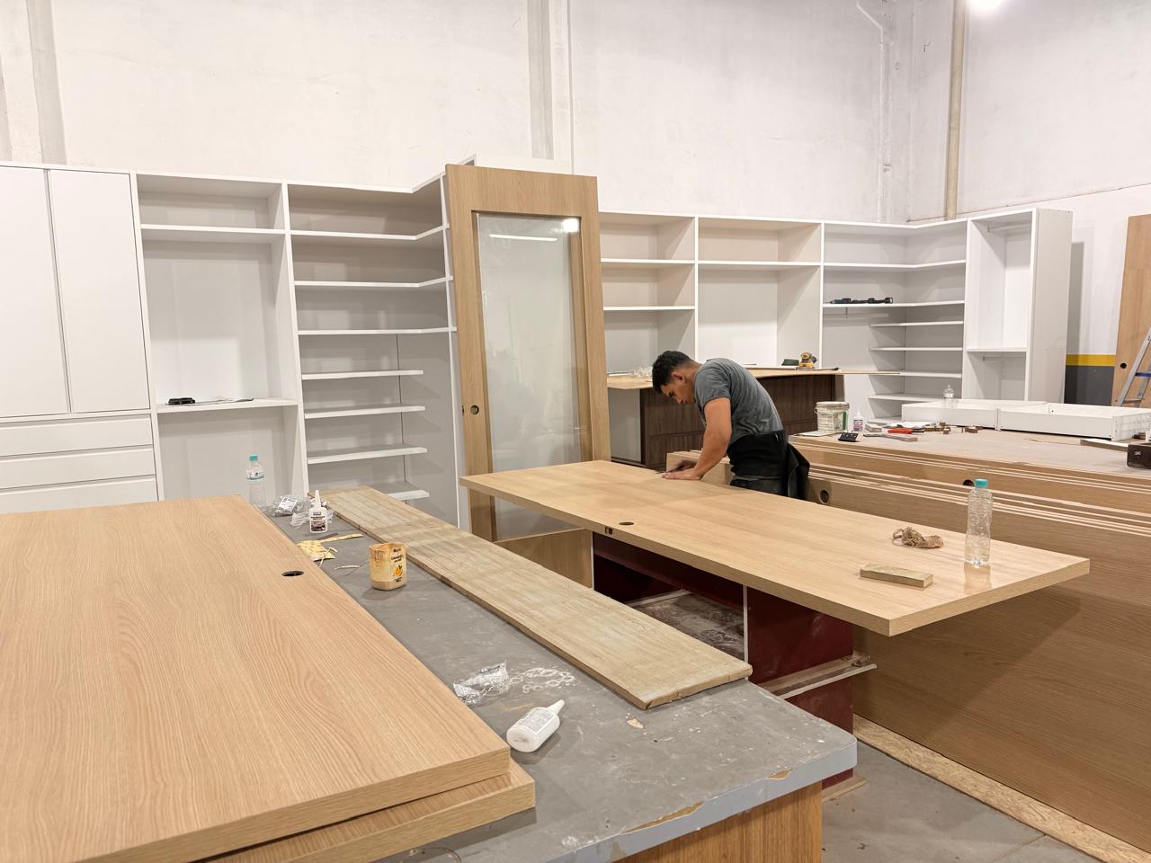 Interior da fábrica da D'Lócus em Itajaí: marceneiro conferindo painéis de lâmina natural com armários brancos ao fundo